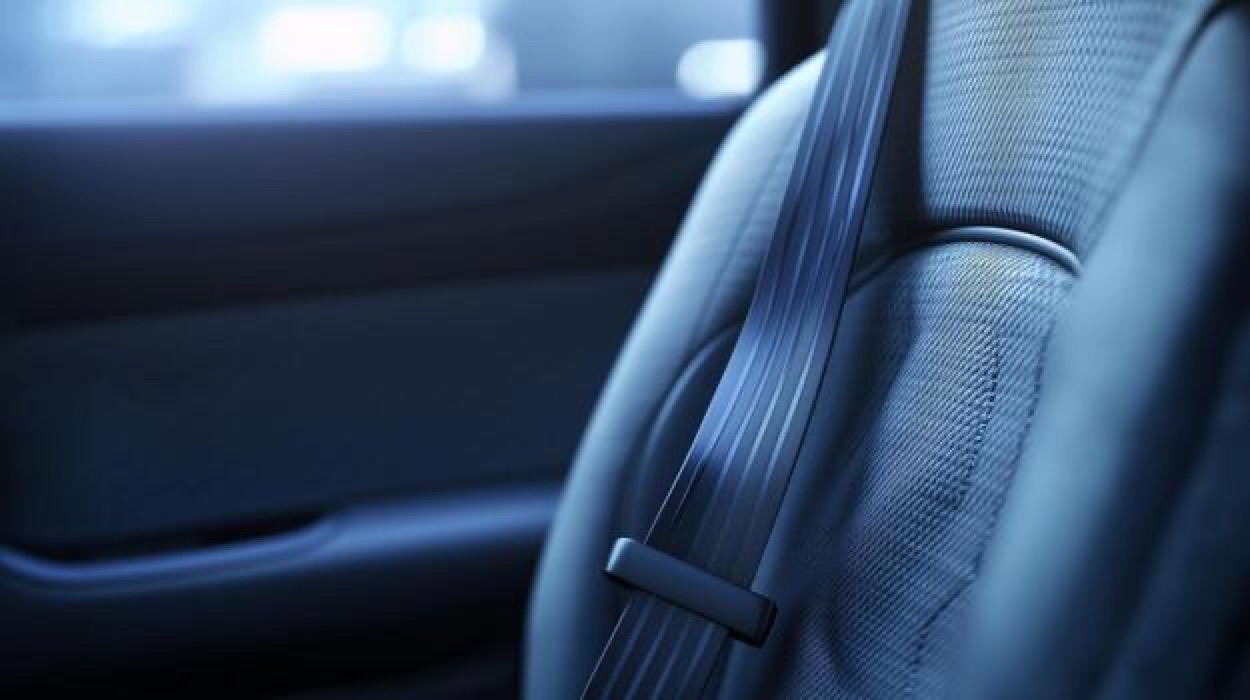 Seatbelt webbing lying diagonally across the shoulder area of a pale vehicle seat in cool interior light.